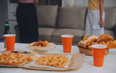 Bir grup genç arkadaş evde pizza ve hazır yemekle parti veriyor.