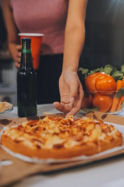 Bir grup genç arkadaş evde pizza ve hazır yemekle parti veriyor.