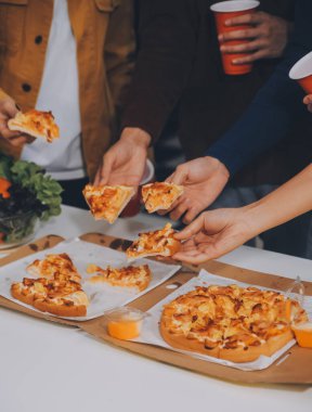 Bir grup genç arkadaş evde pizza ve hazır yemekle parti veriyor.