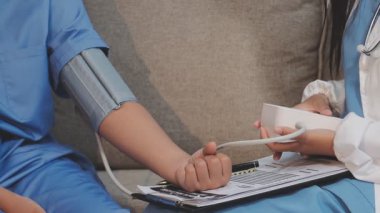 Kanepede kadının tansiyonunu ölçmeye yardım eden Asyalı doktor.