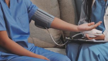 Kanepede kadının tansiyonunu ölçmeye yardım eden Asyalı doktor.
