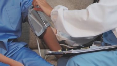 Kanepede kadının tansiyonunu ölçmeye yardım eden Asyalı doktor.