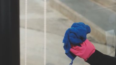 Genç Asyalı kadın modern ofiste sprey ve bezle pencereyi temizliyor.