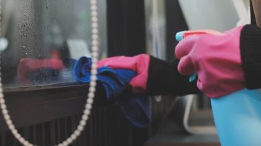 Genç Asyalı kadın modern ofiste sprey ve bezle pencereyi temizliyor.