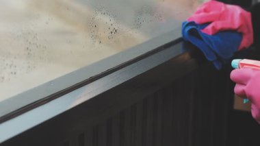 Genç Asyalı kadın modern ofiste sprey ve bezle pencereyi temizliyor.