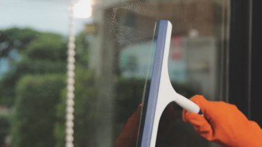Modern ofisin penceresinden suyu silmek için Squeegee kullanan Asyalı kadın.