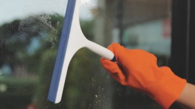 Modern ofisin penceresinden suyu silmek için Squeegee kullanan Asyalı kadın.