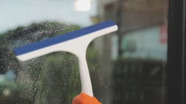 Modern ofisin penceresinden suyu silmek için Squeegee kullanan Asyalı kadın.