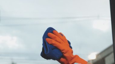 Genç Asyalı kadın modern ofiste sprey ve bezle pencereyi temizliyor.