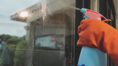 Genç Asyalı kadın modern ofiste sprey ve bezle pencereyi temizliyor.