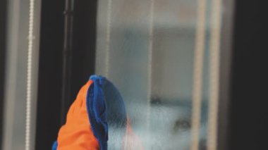 Genç Asyalı kadın modern ofiste sprey ve bezle pencereyi temizliyor.