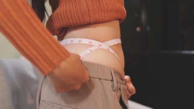 Şişman göbeğini mutfakta bir mezura ile ölçen bir kadın.