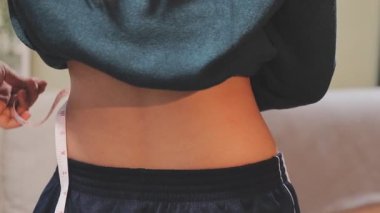 Evinde ölçü bandıyla belini ölçen genç bir kadın.