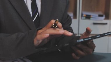 Asyalı işadamı, modern bir ofis ortamındaki tablet üzerindeki mali belgeleri ve grafikleri analiz ediyor.