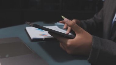 Asyalı işadamı, modern bir ofis ortamındaki tablet üzerindeki mali belgeleri ve grafikleri analiz ediyor.