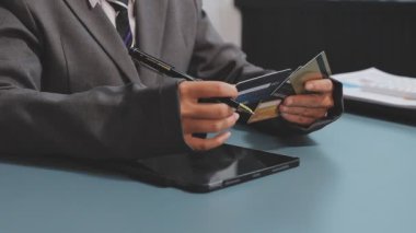 Asyalı takım elbiseli genç iş kadınının kredi kartı numarasını tablete girerken yakın plan görüntüsü.