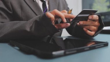 Asyalı takım elbiseli genç iş kadınının kredi kartı numarasını tablete girerken yakın plan görüntüsü.