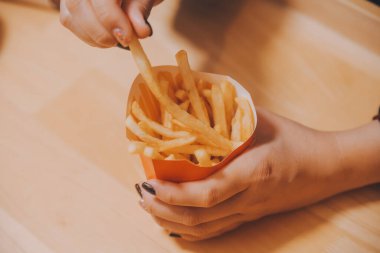 Asyalı kadın elinde patates kızartması ve restoranda mutlu bir şekilde yemek yiyor.