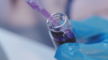 Genç bayan araştırmacı modern bir laboratuarda kimyasal sıvıları yakından inceliyor..