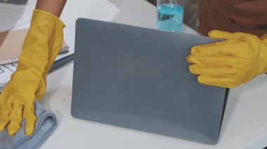 Eldivenli bir kadın bilgisayarını paçavrayla temizliyor.