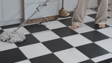 Kadın elektrikli süpürgeyle modern mutfağı temizliyor.