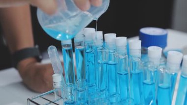 Laboratuvarda elinde mavi sıvıyla bir pipet tutan bilim adamının resmi..