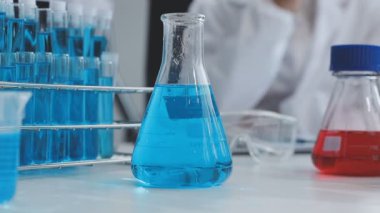 Mavi üniformalı laboratuvar asistanı elinde cam şişe ve sıvı tutuyor. Laboratuvarda laboratuvar asistanı