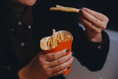 Asyalı kadın elinde patates kızartması ve restoranda mutlu bir şekilde yemek yiyor.