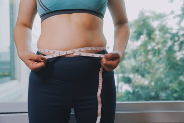 Şişman kadın, şişko, obez kadın el ele tutuşan ölçü bandıyla göbek yağı, kadın diyeti yaşam tarzı konsepti