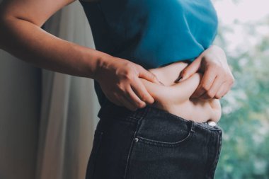 Şişman kadın, şişko, obez kadın el ele tutuşan ölçü bandıyla göbek yağı, kadın diyeti yaşam tarzı konsepti