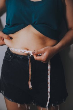 Şişman kadın, şişko, obez kadın el ele tutuşan ölçü bandıyla göbek yağı, kadın diyeti yaşam tarzı konsepti