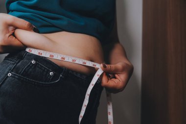 Şişman kadın, şişko, obez kadın el ele tutuşan ölçü bandıyla göbek yağı, kadın diyeti yaşam tarzı konsepti
