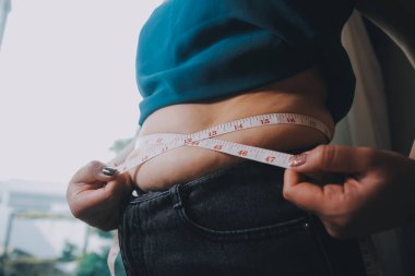 Şişman kadın, şişko, obez kadın el ele tutuşan ölçü bandıyla göbek yağı, kadın diyeti yaşam tarzı konsepti