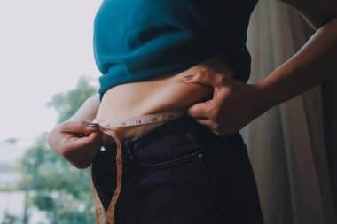 Şişman kadın, şişko, obez kadın el ele tutuşan ölçü bandıyla göbek yağı, kadın diyeti yaşam tarzı konsepti
