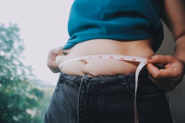 Şişman kadın, şişko, obez kadın el ele tutuşan ölçü bandıyla göbek yağı, kadın diyeti yaşam tarzı konsepti