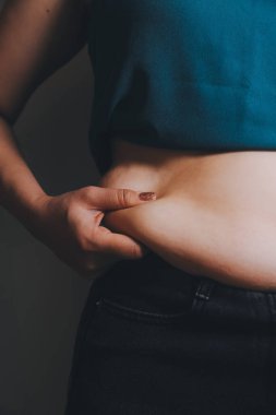 Şişman kadın, şişko, obez kadın el ele tutuşan ölçü bandıyla göbek yağı, kadın diyeti yaşam tarzı konsepti