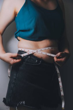 Şişman kadın, şişko, obez kadın el ele tutuşan ölçü bandıyla göbek yağı, kadın diyeti yaşam tarzı konsepti