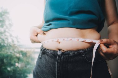 Şişman kadın, şişko, obez kadın el ele tutuşan ölçü bandıyla göbek yağı, kadın diyeti yaşam tarzı konsepti