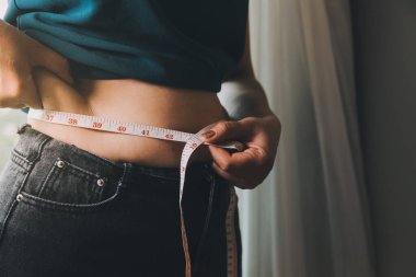 Şişman kadın, şişko, obez kadın el ele tutuşan ölçü bandıyla göbek yağı, kadın diyeti yaşam tarzı konsepti