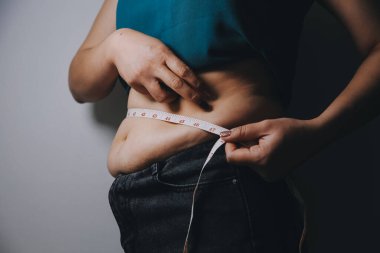 Şişman kadın, şişko, obez kadın el ele tutuşan ölçü bandıyla göbek yağı, kadın diyeti yaşam tarzı konsepti