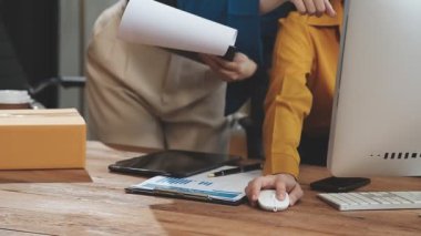 Bir depo dolusu karton kutuyla birlikte mali raporları inceleyen kadın uzmanlar online alışveriş endüstrisini vurguluyorlar..