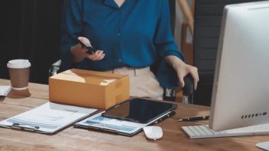 İşyeri sahibi internetten bilgisayarını kontrol ediyor ve ürününü masada kontrol ediyor.