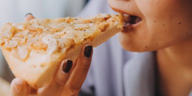 Restoranda pizza dilimi tutan bir kadın resmi.