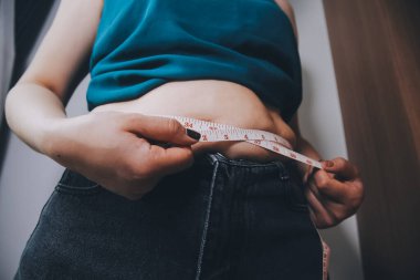 Şişman kadın, şişko, obez kadın el ele tutuşan ölçü bandıyla göbek yağı, kadın diyeti yaşam tarzı konsepti