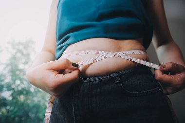 Şişman kadın, şişko, obez kadın el ele tutuşan ölçü bandıyla göbek yağı, kadın diyeti yaşam tarzı konsepti