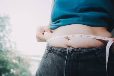 Şişman kadın, şişko, obez kadın el ele tutuşan ölçü bandıyla göbek yağı, kadın diyeti yaşam tarzı konsepti
