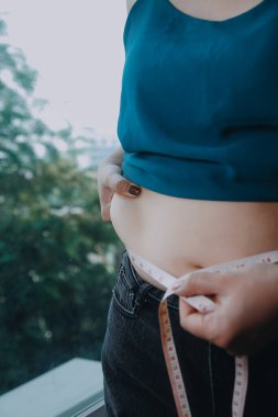 Şişman kadın, şişko, obez kadın el ele tutuşan ölçü bandıyla göbek yağı, kadın diyeti yaşam tarzı konsepti