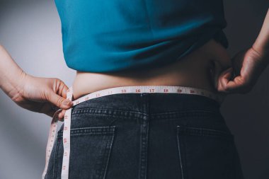 Şişman kadın, şişko, obez kadın el ele tutuşan ölçü bandıyla göbek yağı, kadın diyeti yaşam tarzı konsepti