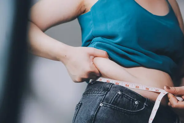 Şişman kadın, şişko, obez kadın el ele tutuşan ölçü bandıyla göbek yağı, kadın diyeti yaşam tarzı konsepti