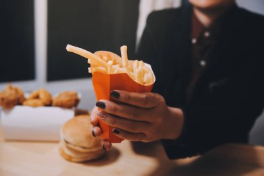 Asyalı kadın elinde patates kızartması ve restoranda mutlu bir şekilde yemek yiyor.